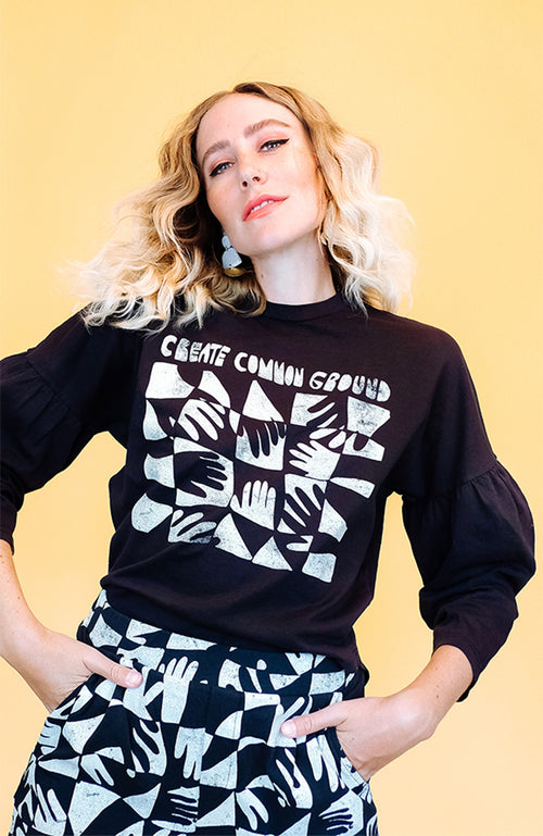 Black three-quarter-length puff sleeve, has a crew neck with a curved hem.  Slightly roomy fit. Has a hand painted "Create Common Ground" graphic.